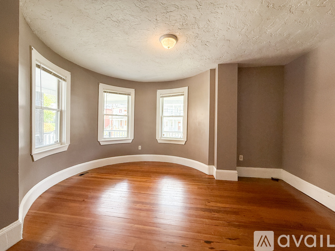 A room with wooden floors and three windows.