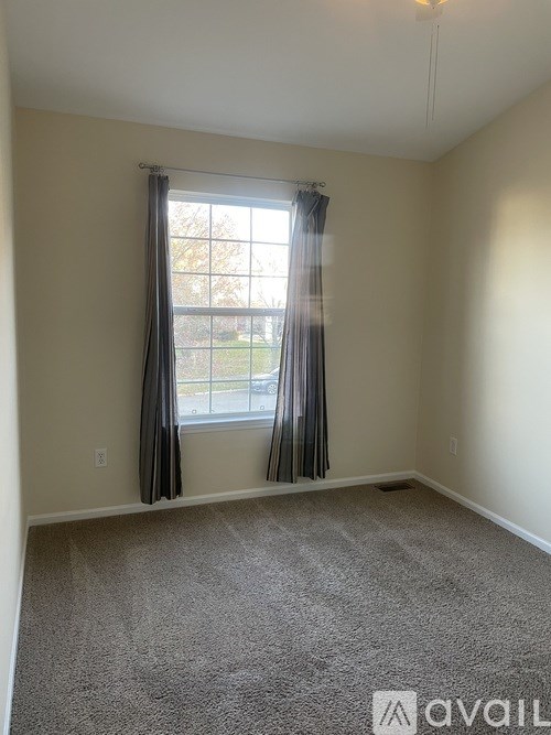 A room with a carpeted floor and a window with curtains.