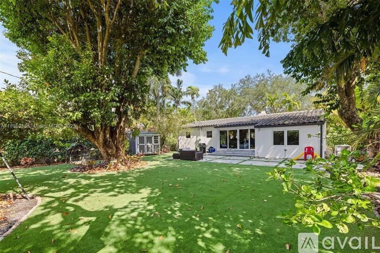 A house with a white exterior is surrounded by a green lawn and trees.