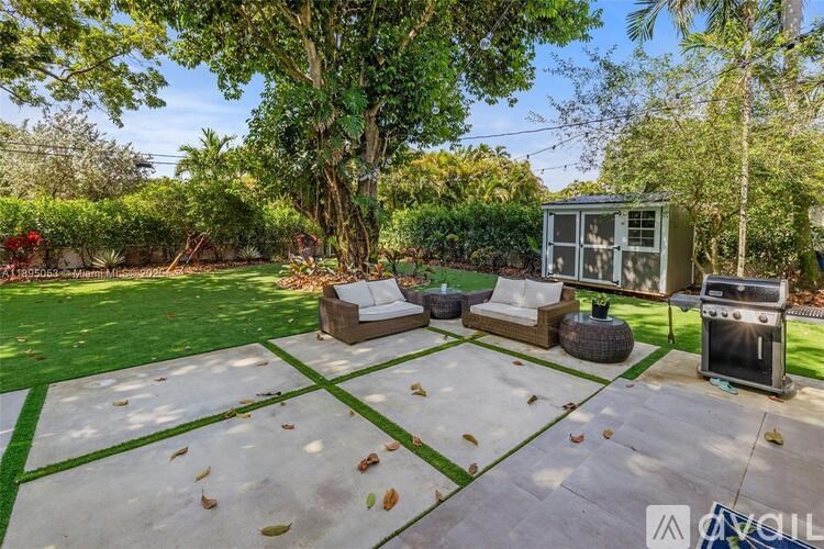 A backyard with a patio, a grill, and a tree.
