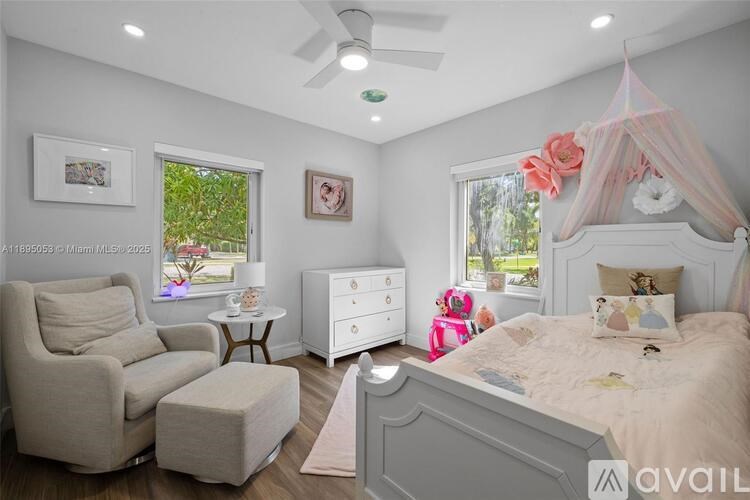 A bedroom with a canopy bed, a chair, a dresser, and a window with a view of trees.
