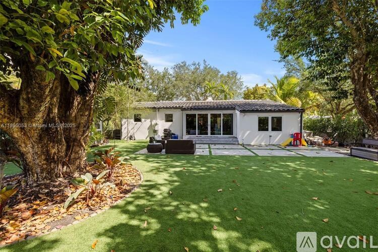 A white house with a black roof is surrounded by greenery.