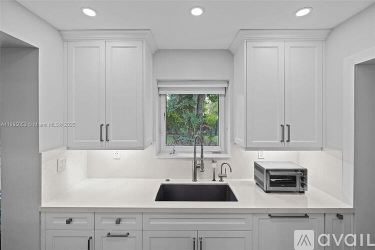 A modern kitchen with white cabinets and a window.