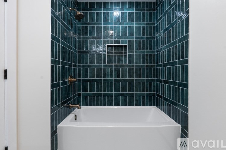 A white bathtub is in a bathroom with blue tiles.