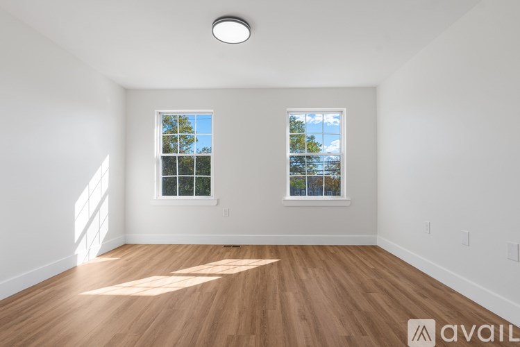 A room with wooden floors and two windows letting in sunlight.