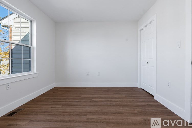 A room with wooden floors and white walls, with a window on the left side.