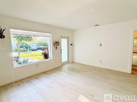 A spacious room with a large window overlooking a garden and a white door.