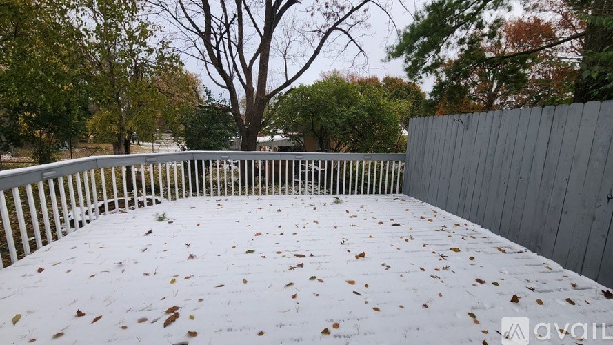A deck with a white railing and fallen leaves on it.