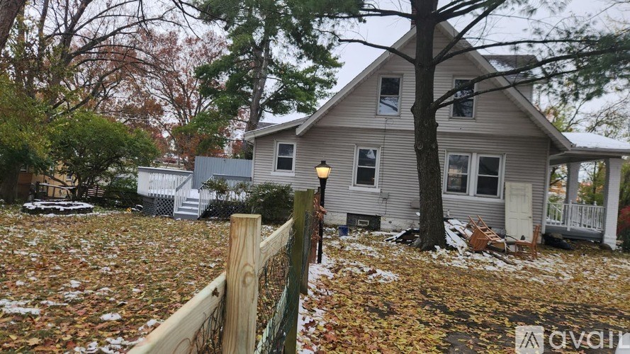 A house with a grey roof and a white fence is surrounded by fallen leaves.