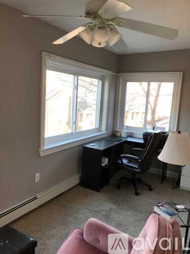 A room with a desk, chairs, and a ceiling fan.