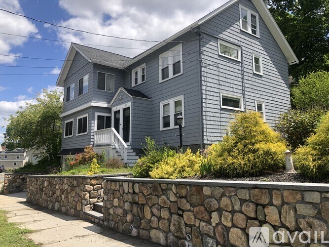 A house with a grey exterior and a stone wall in front.