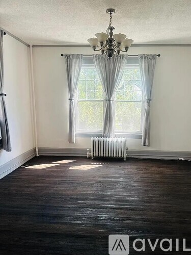 A room with a chandelier, a window with curtains, and a radiator.