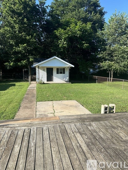 A small white house with a grey roof is surrounded by a wooden deck and a green lawn.