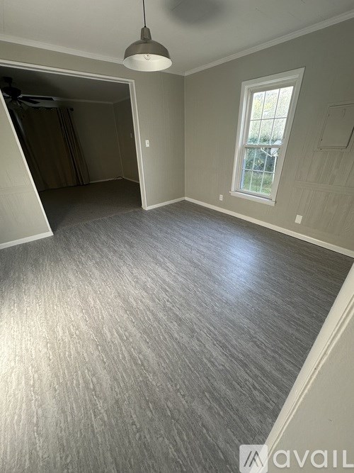 A room with a grey carpet and a window with a white frame.