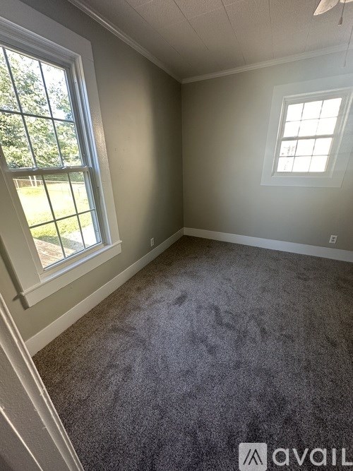 A room with a carpeted floor and two windows.