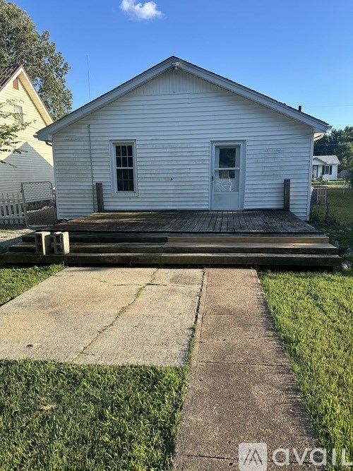 A small white building with a porch and a concrete walkway leading to it.
