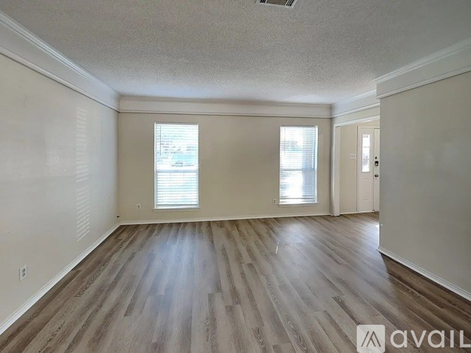 A spacious room with wooden flooring and two windows.