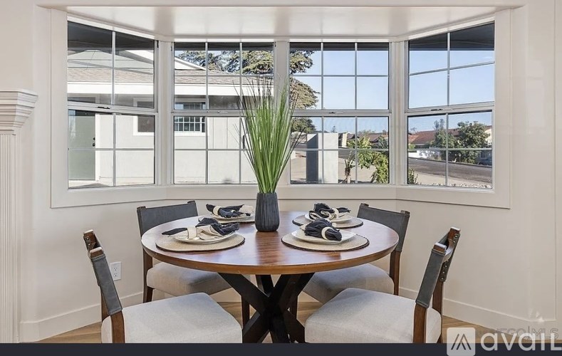 A dining table set with chairs and a vase of grass in front of a window.