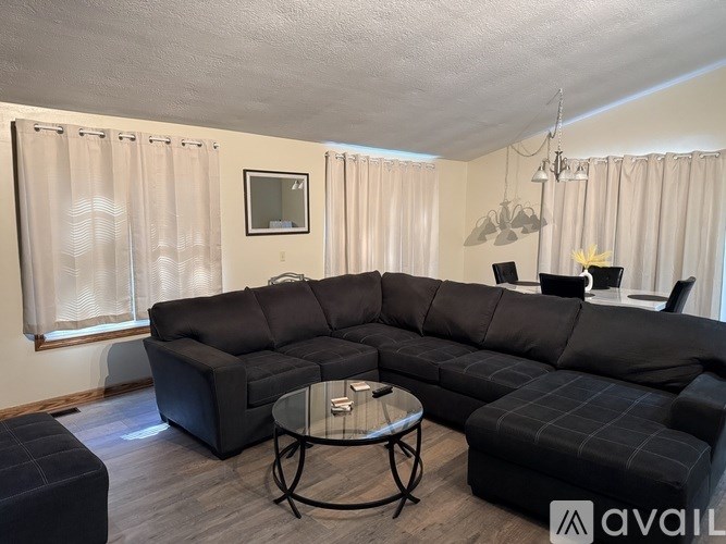A black sectional sofa with a glass table in the middle of the room.