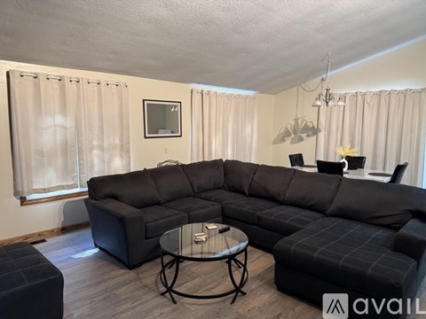 A black sectional sofa with a glass table in the middle of the room.