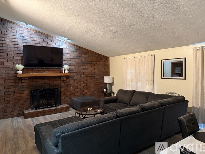 A living room with a grey couch and a brick fireplace.