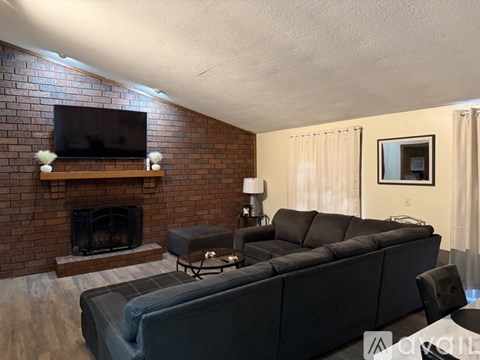 A living room with a grey couch and a brick fireplace.