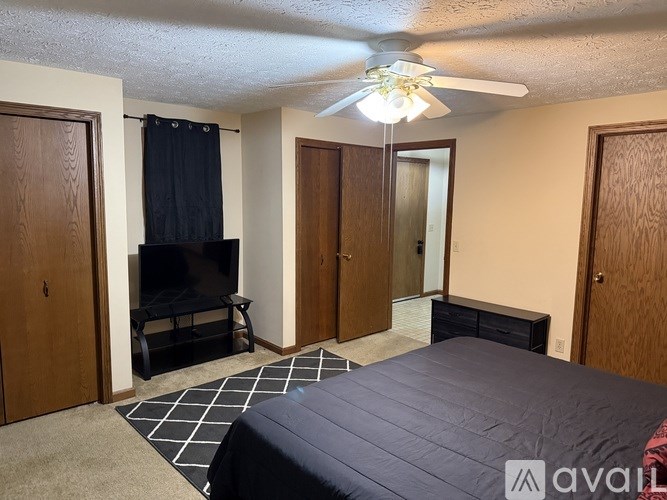 A bedroom with a bed, a television, and a ceiling fan.