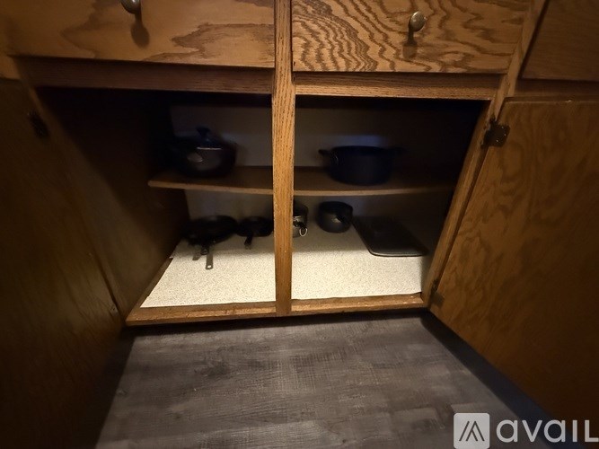 A wooden cabinet with two open doors revealing two shelves with pots and pans.