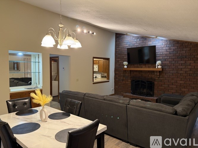 A living room with a grey couch, a white dining table, and a brick fireplace.