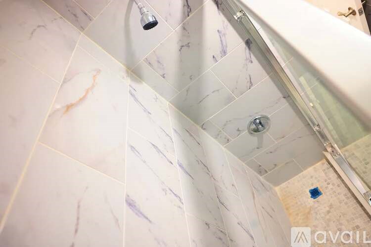 A shower area with a glass door and a marble tile wall.