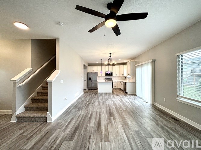 A spacious living room with a staircase on the left and a kitchen area in the background.