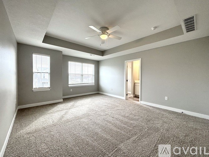 A spacious room with a carpeted floor, a ceiling fan, and a door leading to another room.