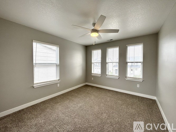 A room with a carpet floor, a ceiling fan, and three windows.