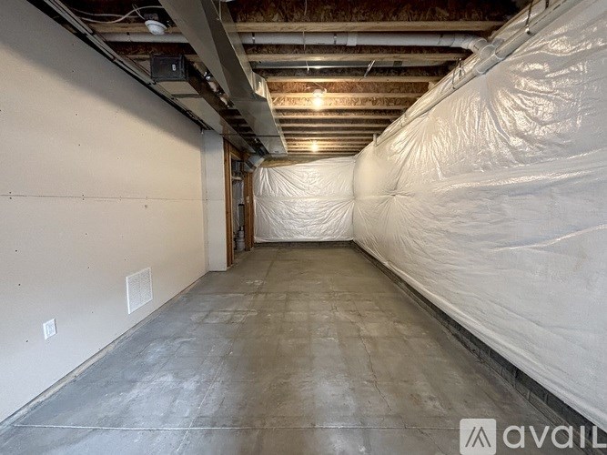 A room with a white wall and a grey floor is covered with white plastic.