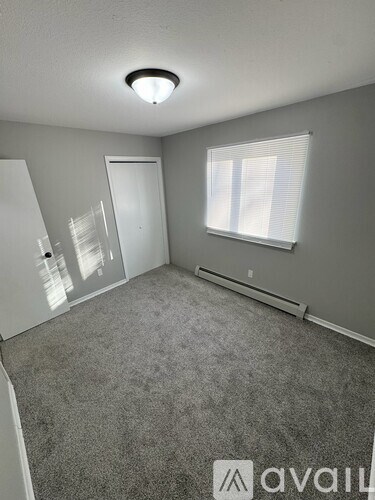 A room with a carpeted floor, a window with blinds, and a door.