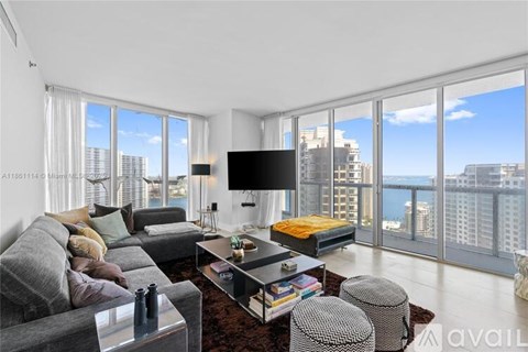 A living room with a grey couch, a coffee table, and a large window overlooking the city.