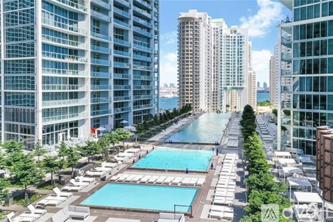 A view of a pool area with a waterfront and buildings in the background.