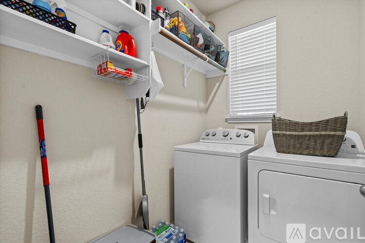 A small laundry room with a washer and dryer, a mop, and a basket on top of the dryer.