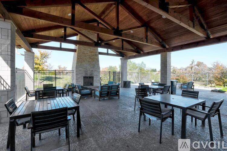 A patio with tables and chairs under a wooden roof.