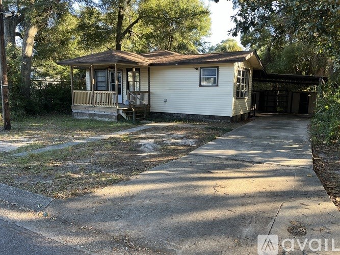 A house with a porch and a covered patio is surrounded by trees.