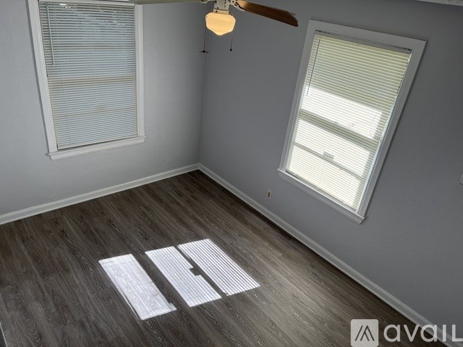 A room with a wooden floor and two windows with blinds.