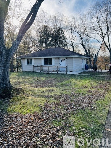 A small white house with a black roof is surrounded by trees and grass.