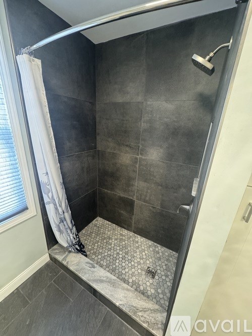 A shower area with a white curtain and a grey tiled floor.