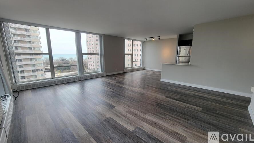 A spacious room with wooden flooring and large windows overlooking a cityscape.