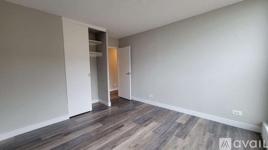 A room with a wooden floor and a white wall with a doorway leading to another room.