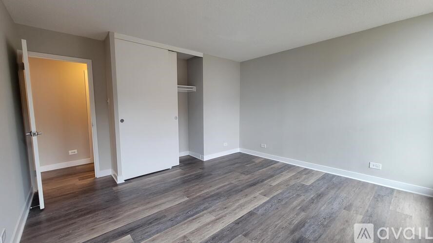 A room with wooden flooring and white walls, with a door on the left and a closet on the right.