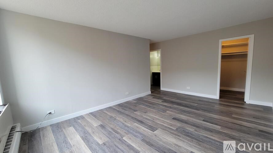 A room with wooden flooring and a white wall with a doorway leading to another room.