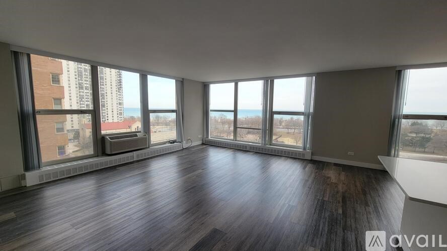 A spacious room with wooden floors and large windows overlooking a cityscape.