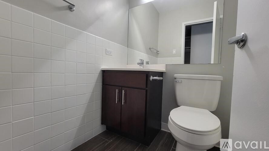 A white toilet sits in a bathroom with a white tiled wall and a brown cabinet.