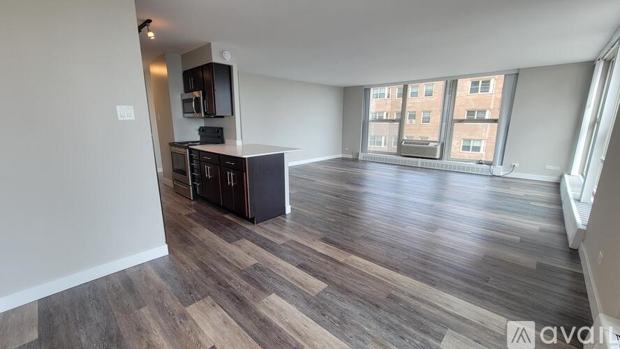 A spacious living room with wood flooring and a kitchen area in the background.